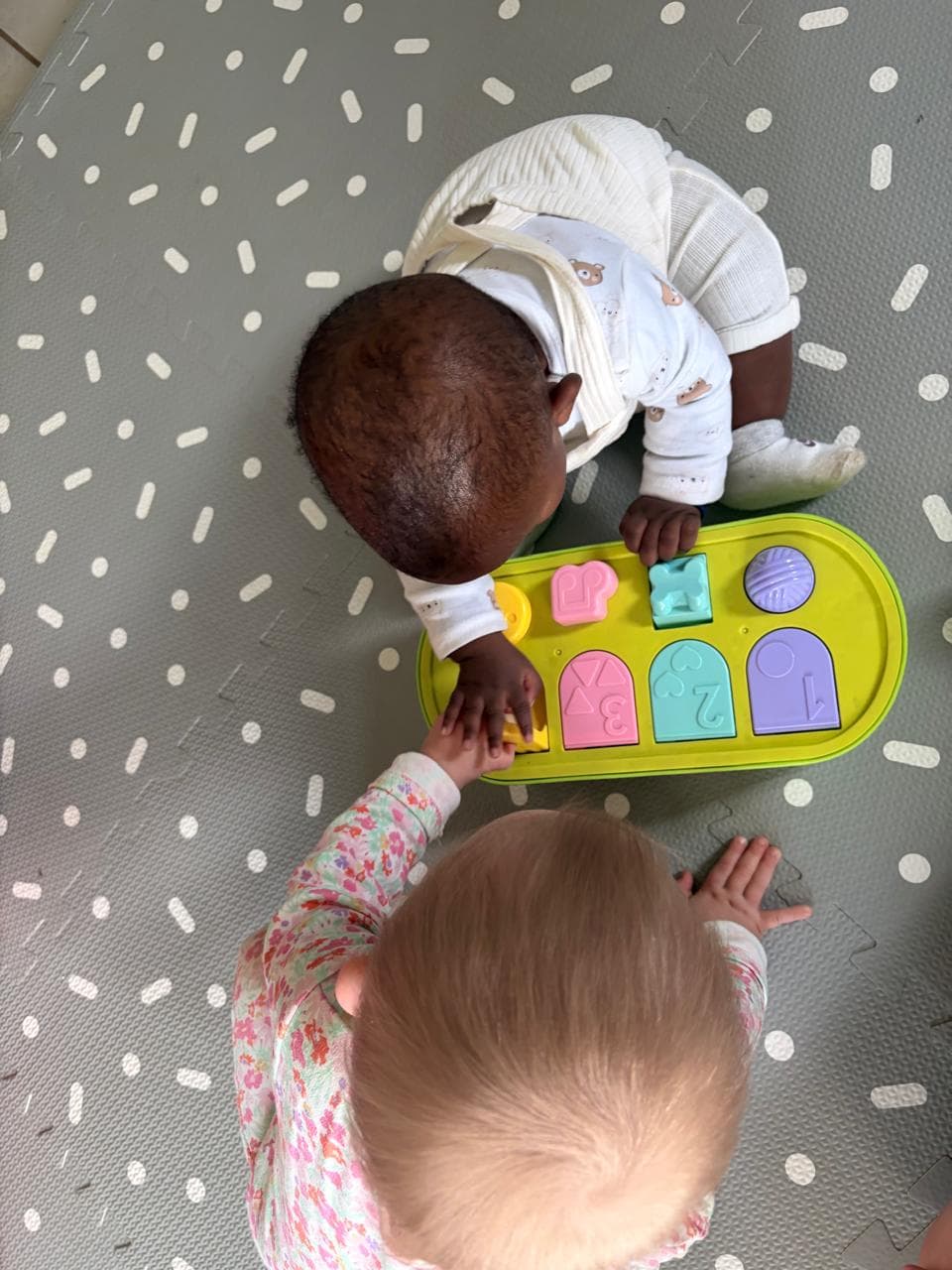 Two babies playing with a shape-sorter toy at the home